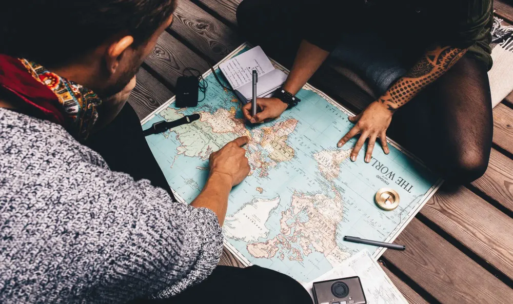 Bird's eye view of couple planning a vacation on a world map while sitting on the floor